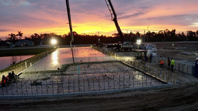 Sunset over a concrete foundation under construction, with rebar and a crane arm silhouetted against the sky