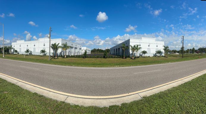 Wide road beside white industrial buildings under a blue sky with clouds