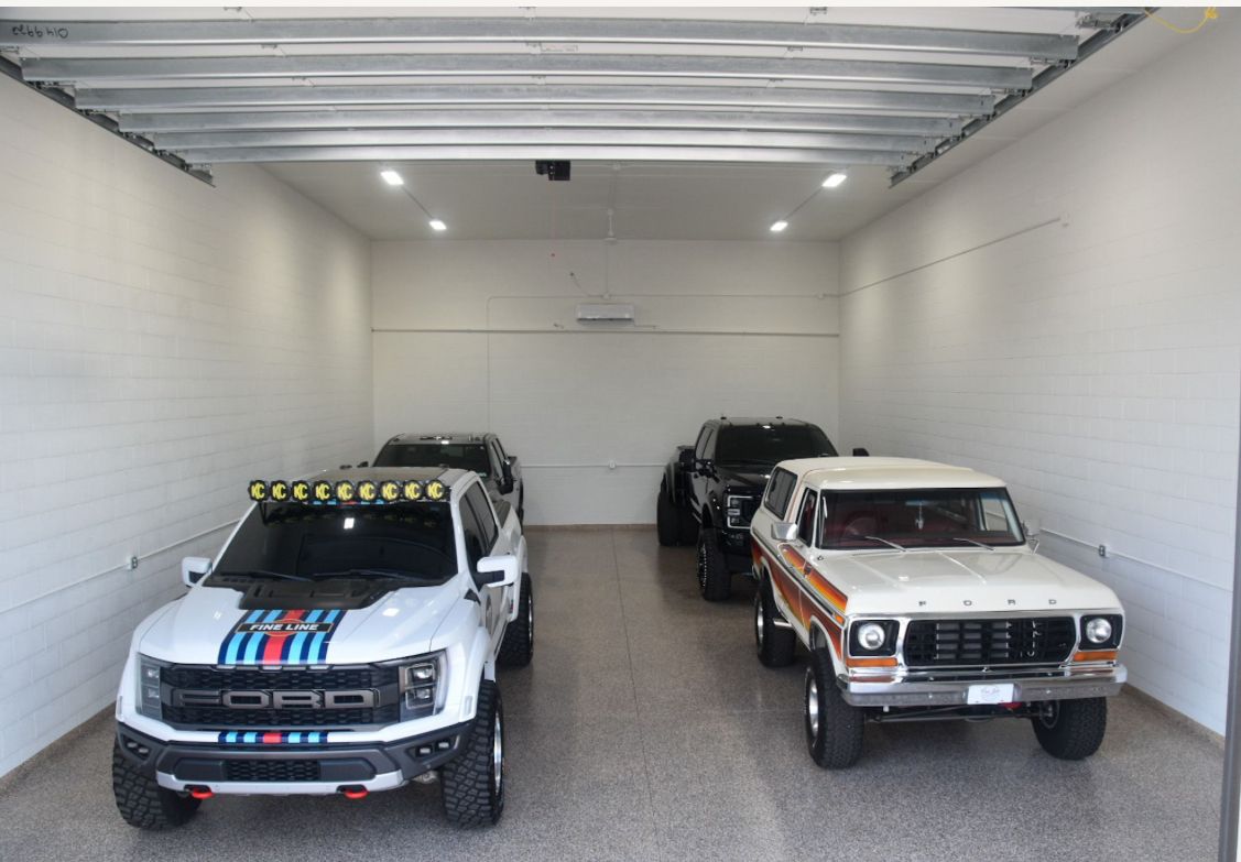 Three off-road trucks parked inside a white garage, including a white racing truck and a white-orange pickup.