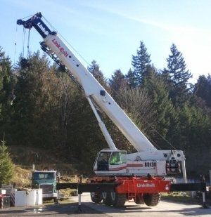 Large white crane truck with extended boom at a wooded worksite