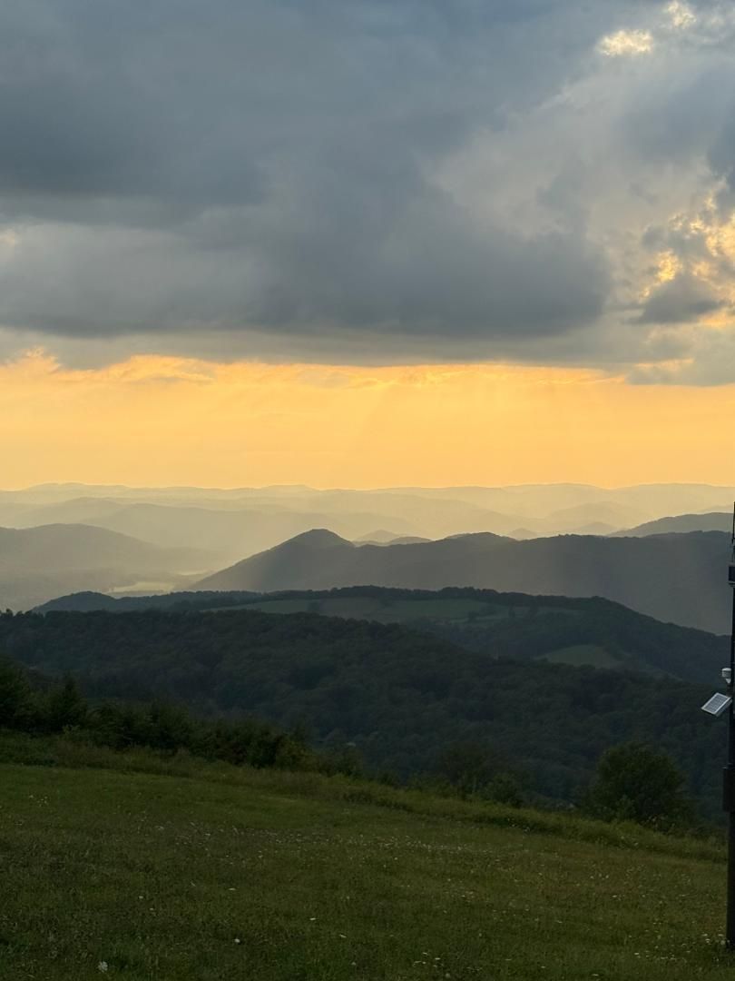 Cloudy sunset over layered mountain ridges and a green hillside