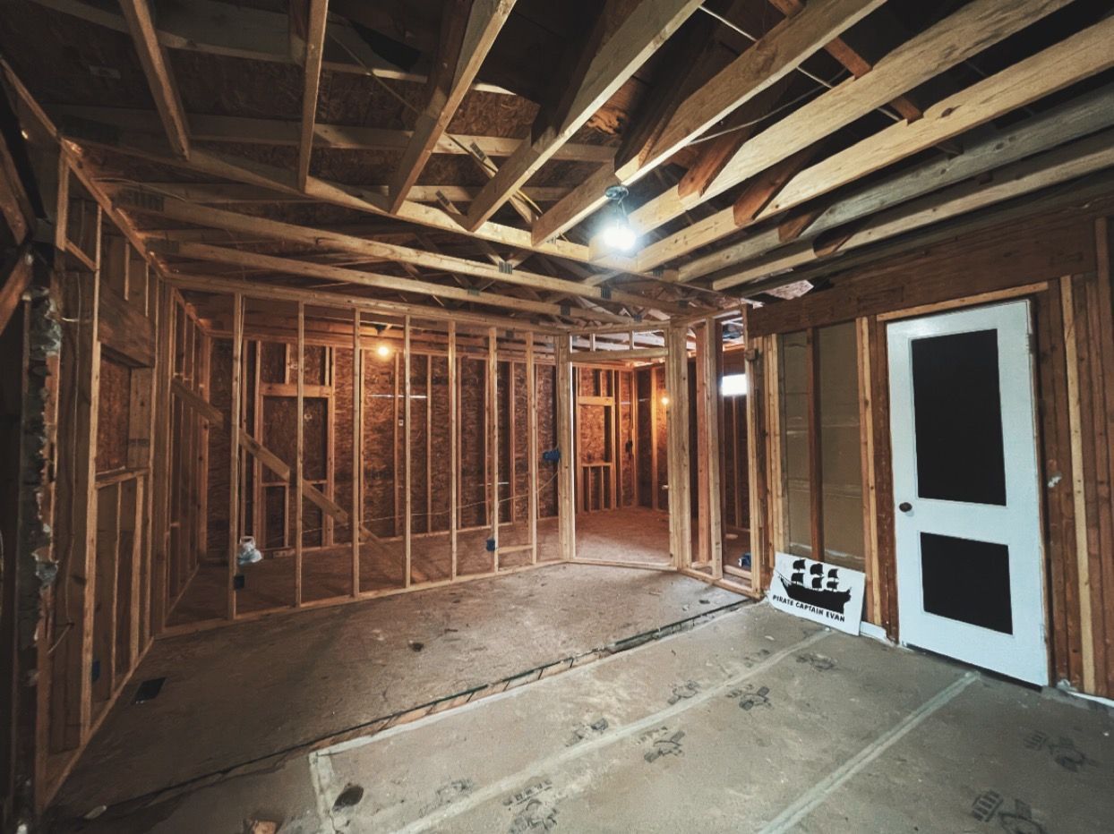 Unfinished basement with exposed wooden framing, joists, and a white door on the right.