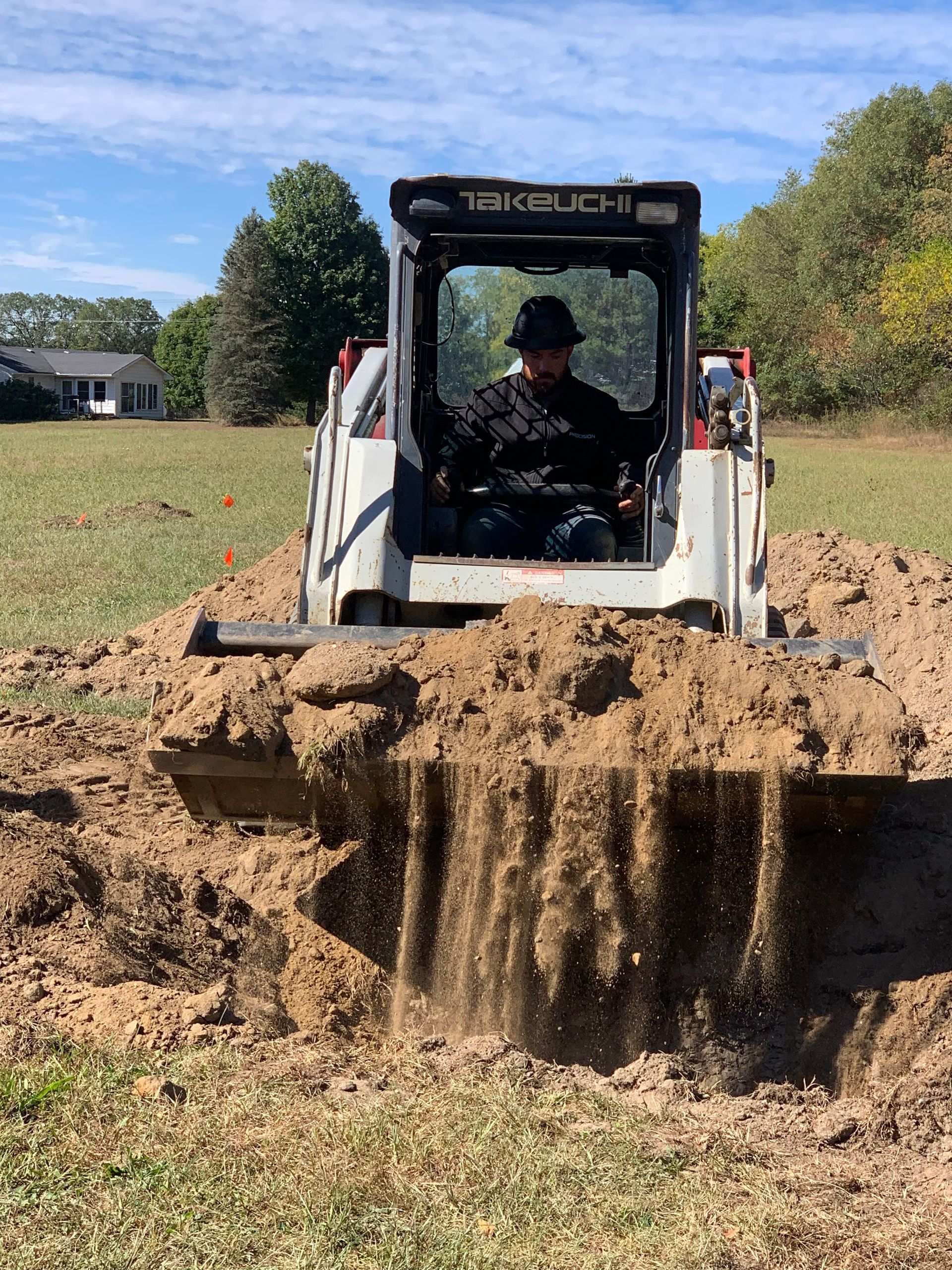 Skid steer loader pushing muddy dirt across a grassy field on a sunny day