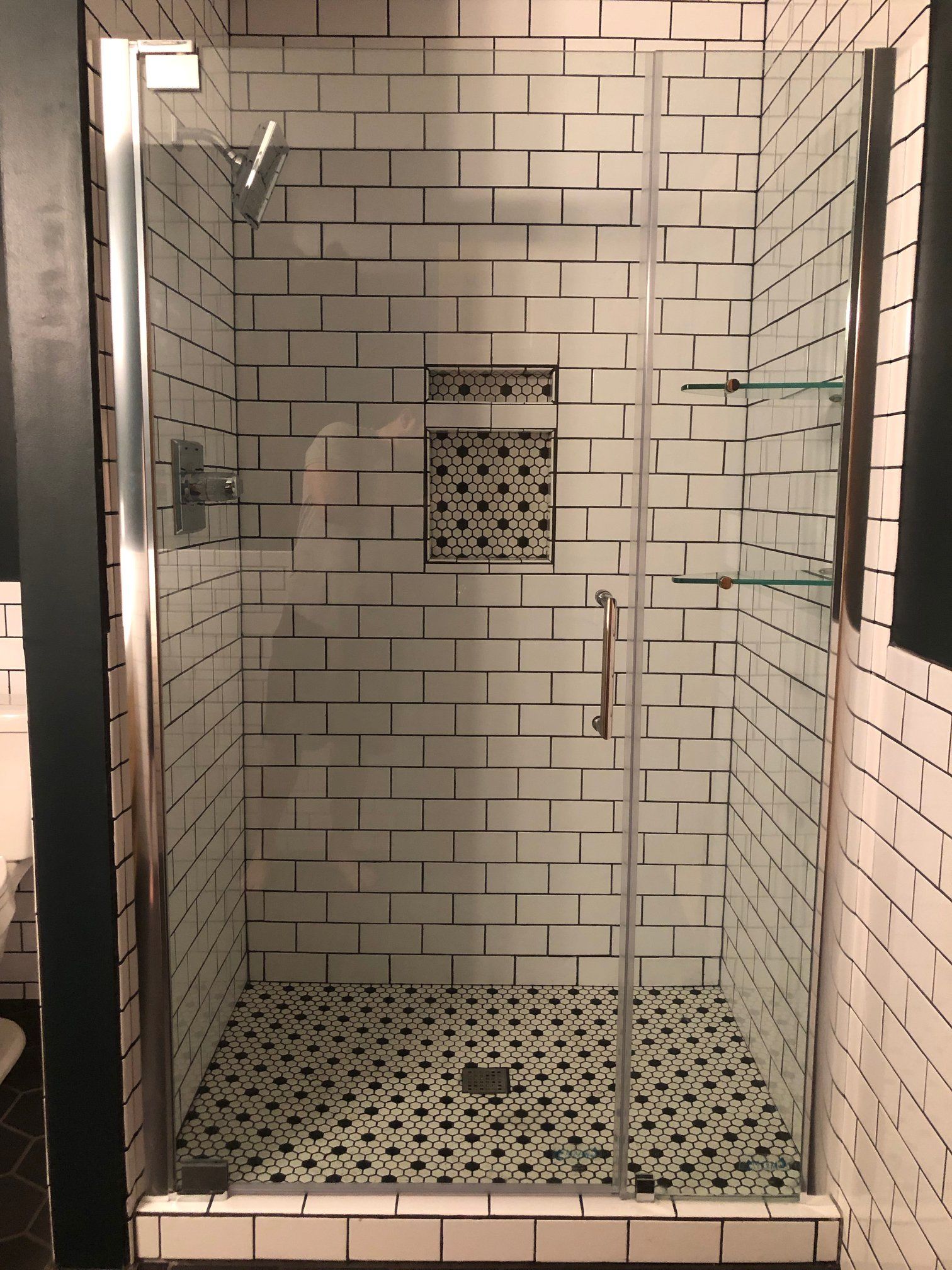 Glass shower stall with white subway tiles and black-and-white mosaic floor and trim