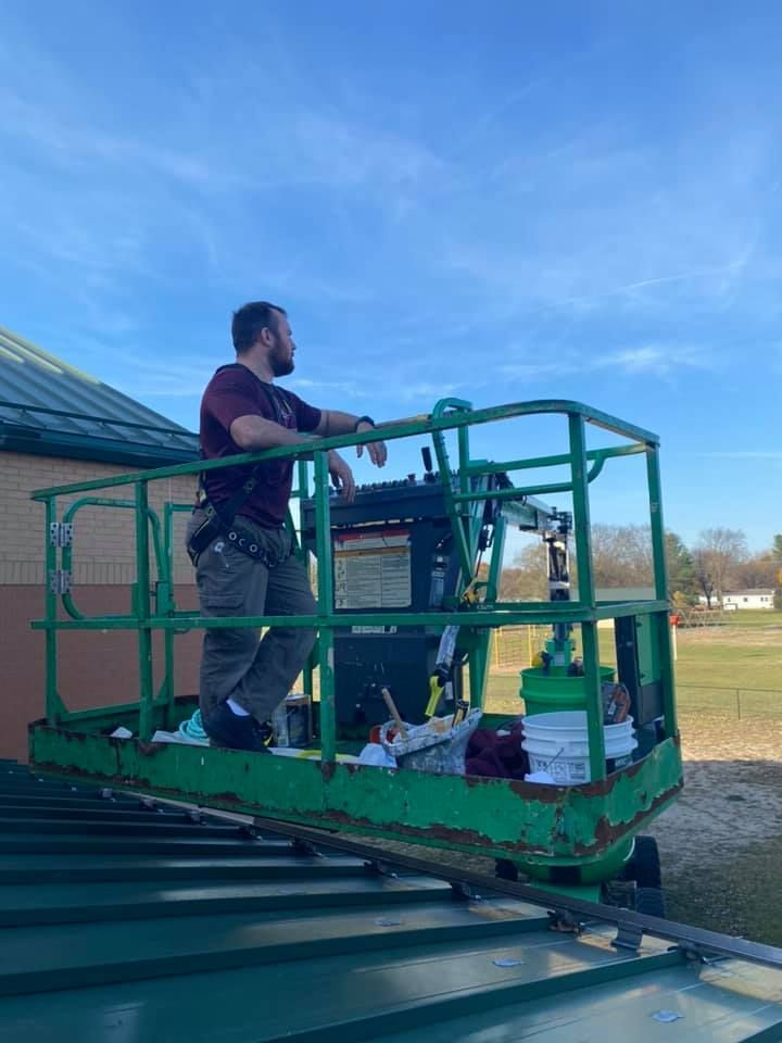 Worker on a green lift platform on a sloped roof under a blue sky