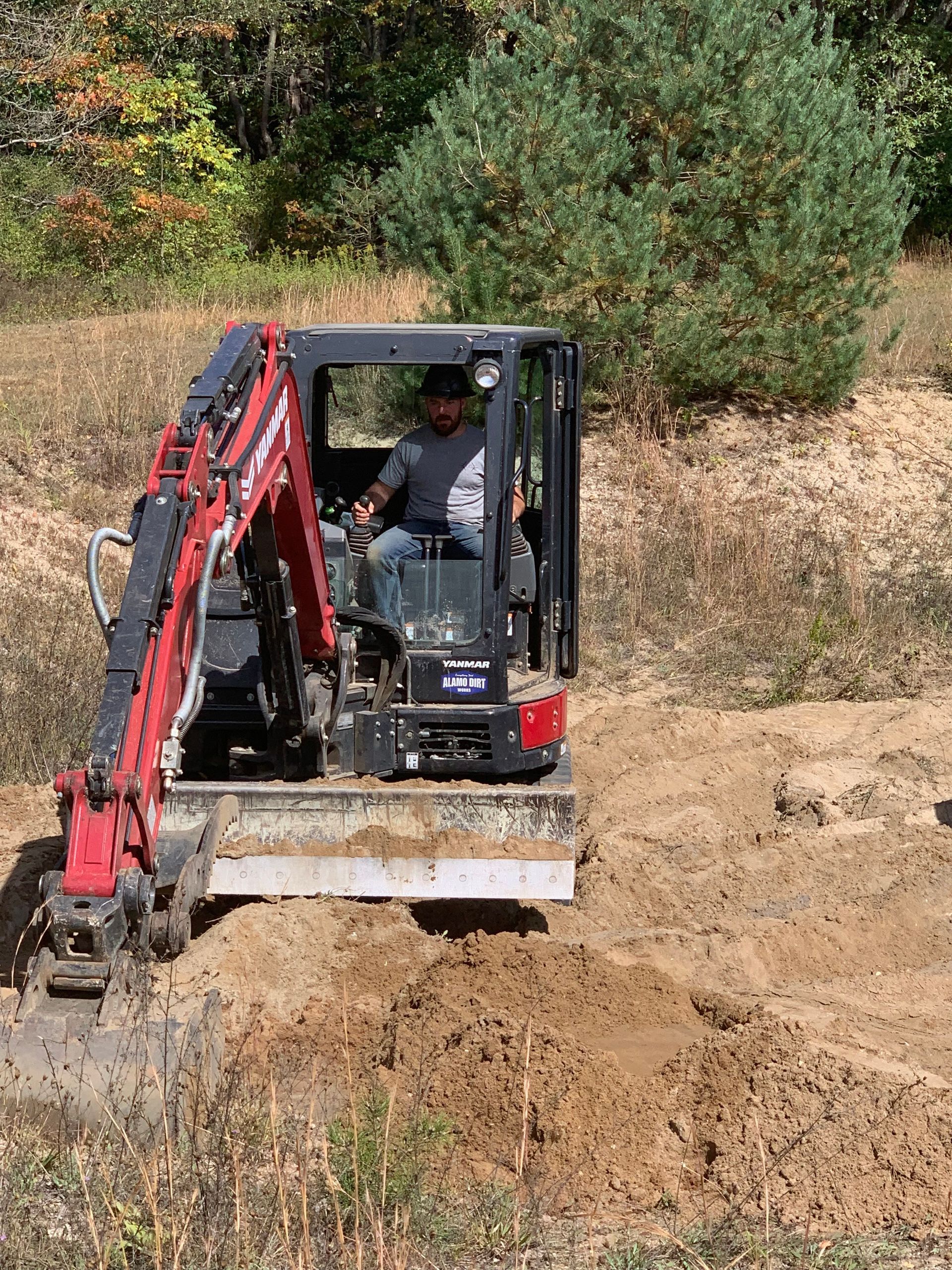 Red mini excavator clearing dirt on a dry hillside with brush in the background