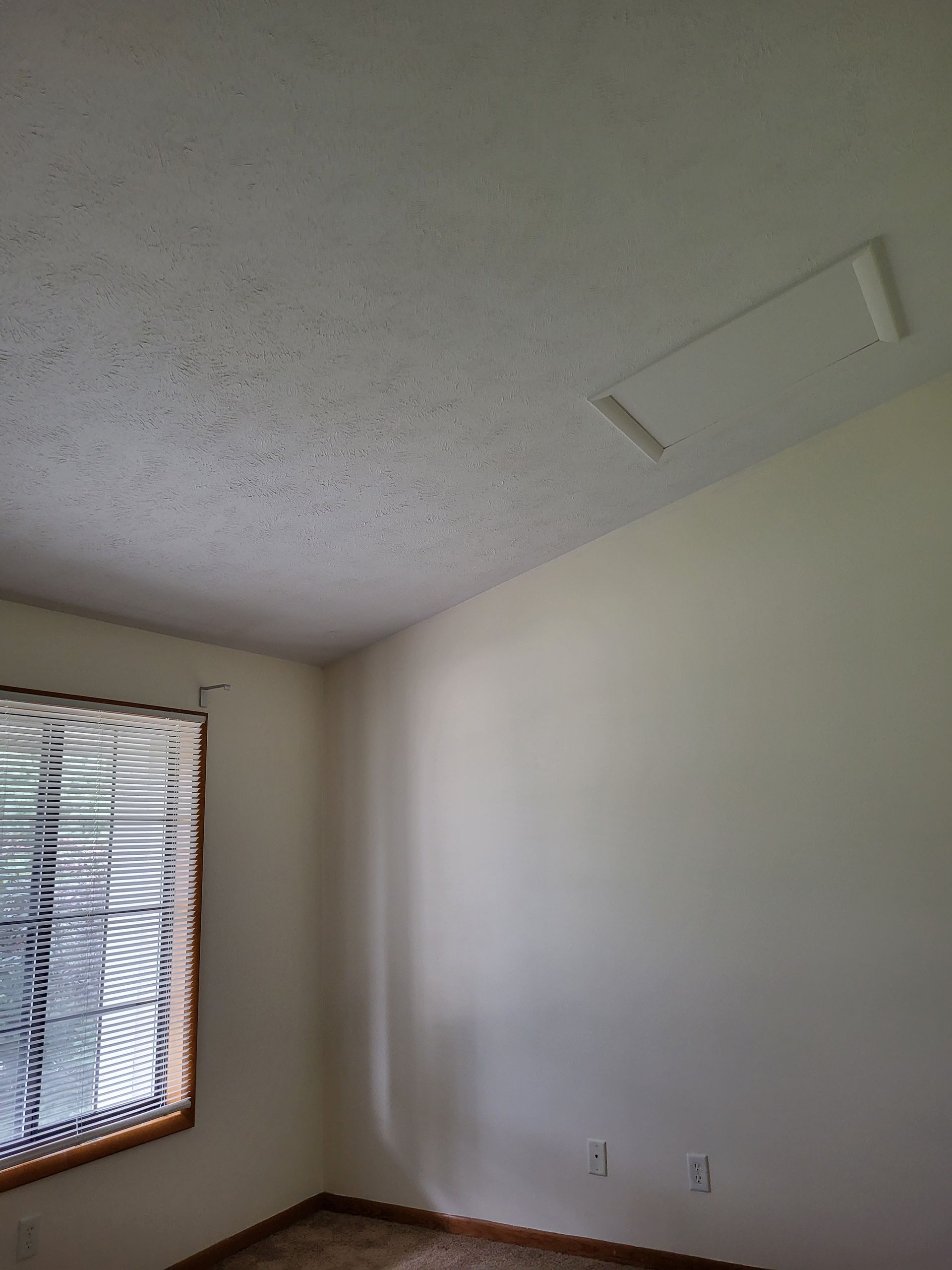 Empty room with white walls, textured ceiling, window blinds, and a small wall light fixture.