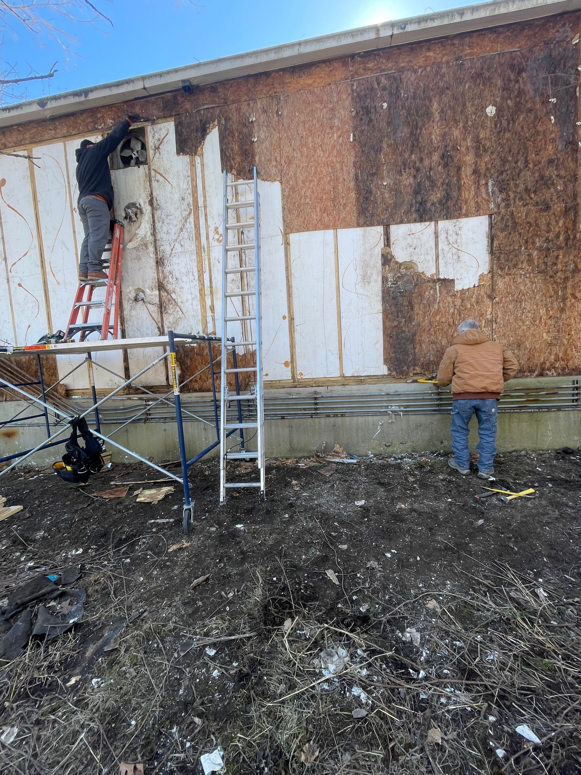 Exterior wall under repair with ladder and scaffolding beside a charred, damaged building facade