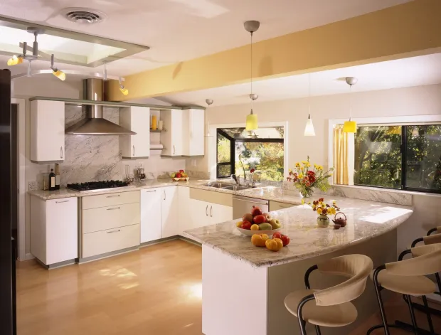 Bright modern kitchen with white cabinets, large island, fruit bowl, and pendant lights by the windows.