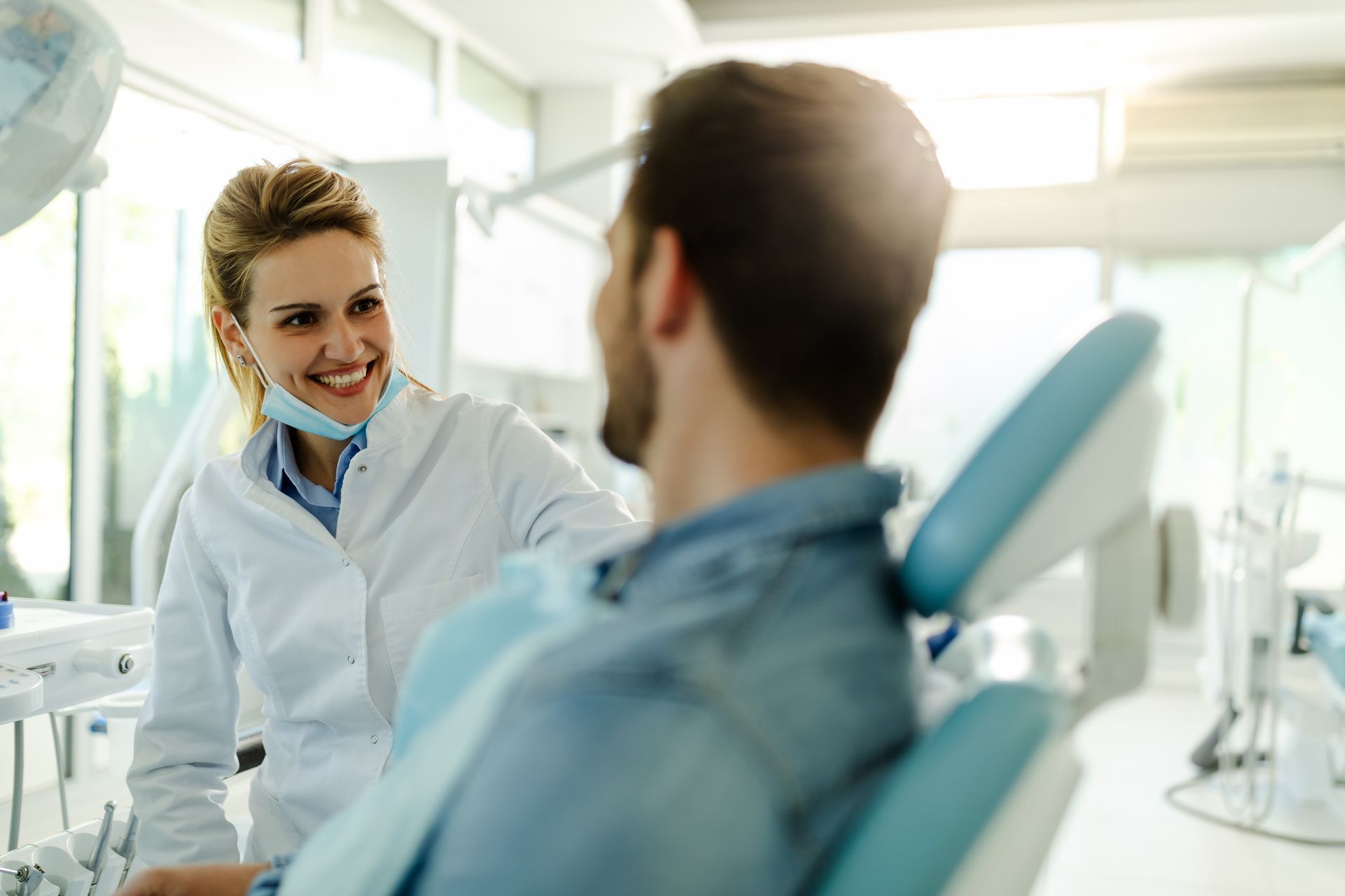 A female dentist is talking with a happy male patient at a clinic.