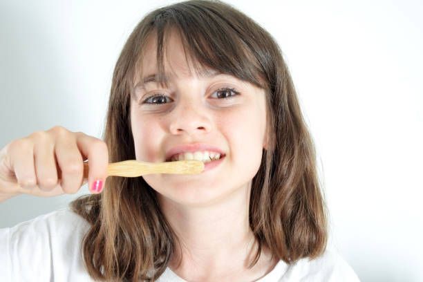 A young girl is brushing her teeth with a wooden toothbrush.