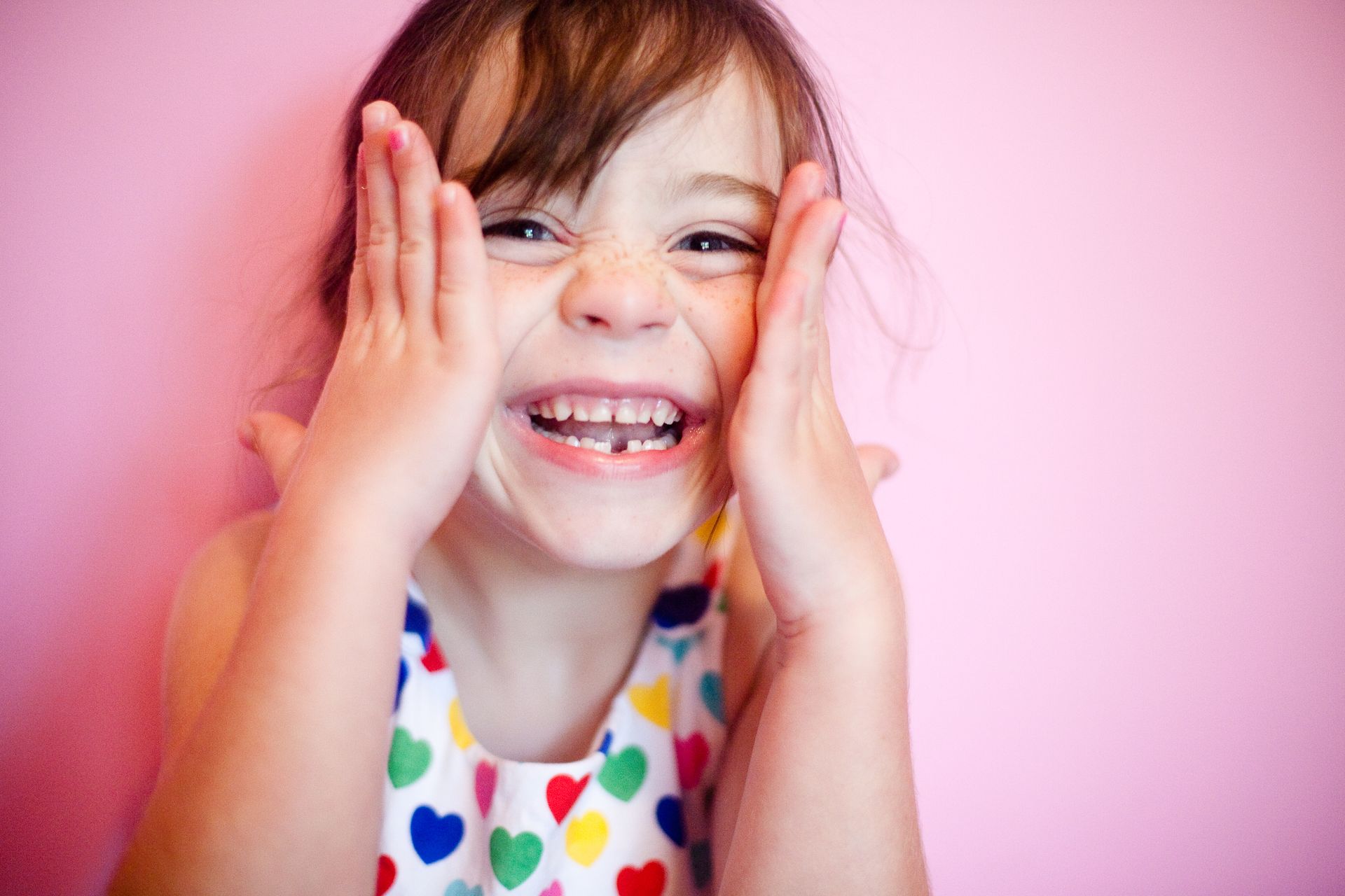 A little girl is covering her face with her hands and smiling.