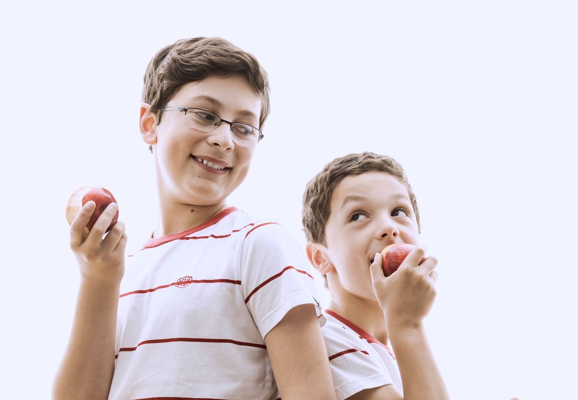 Two people wearing striped shirts stand back-to-back against a white background, each holding an apple.