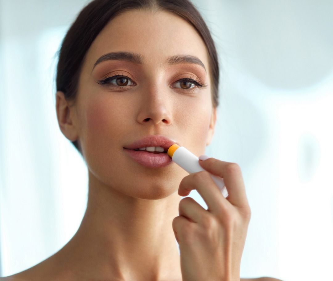 A person applying yellow lip balm from a white tube to their lips.