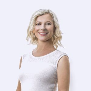 A smiling person with shoulder-length blonde hair, wearing a sleeveless white top, centered against a plain light background.