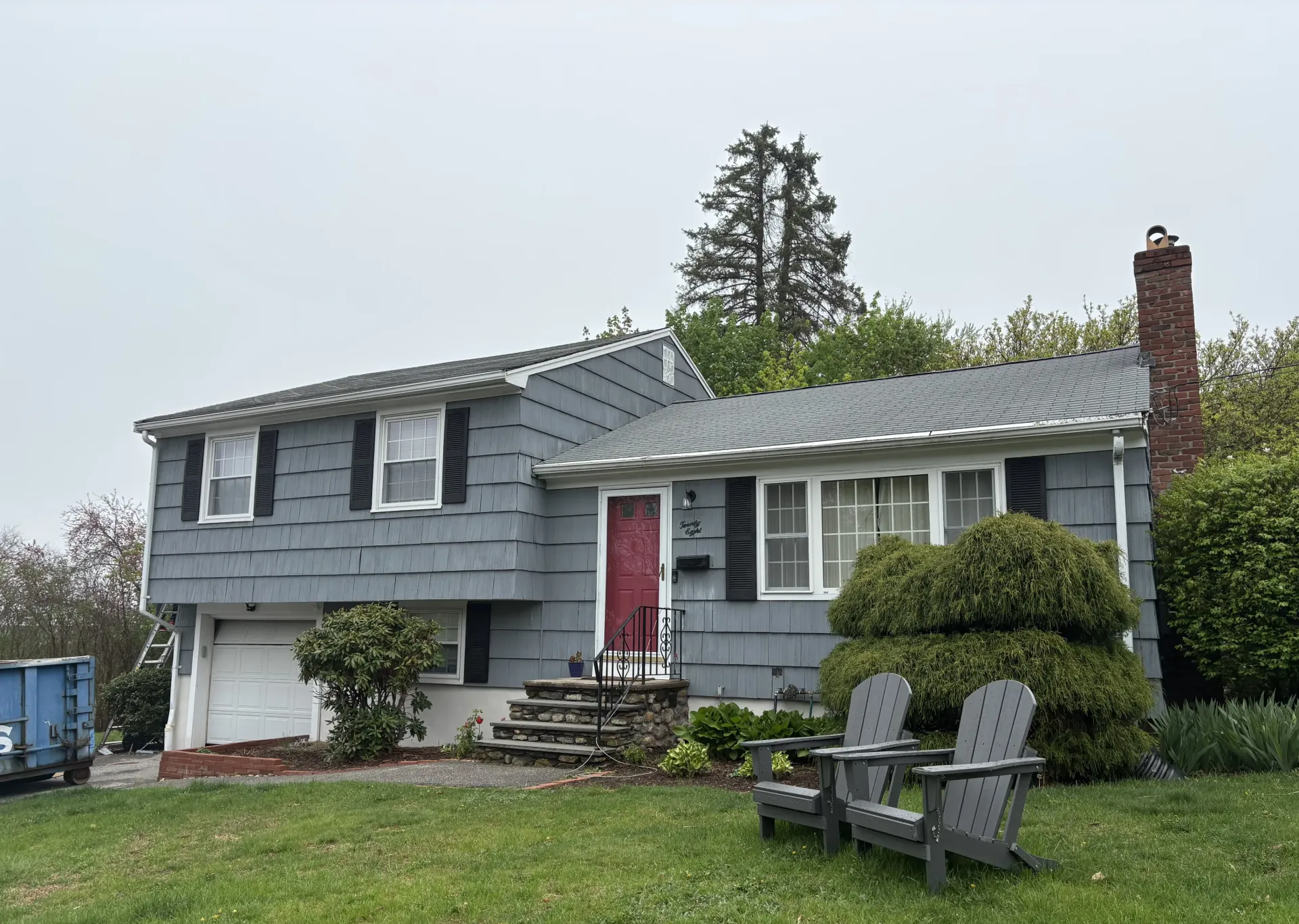 Gray house with red door, black shutters, and two gray chairs on the lawn.