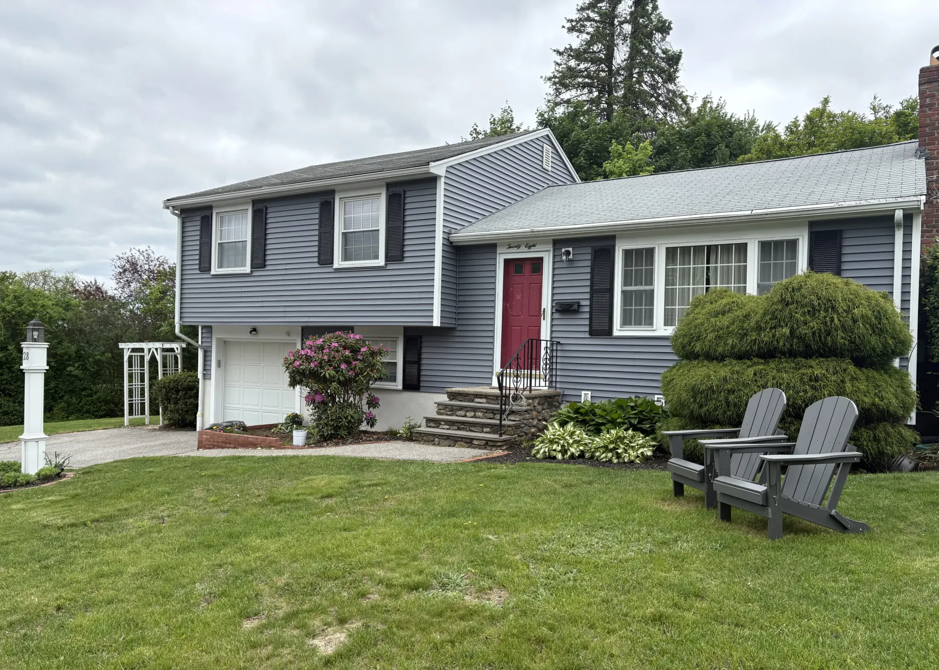 Gray house with red door, shutters, and two gray Adirondack chairs on lawn.