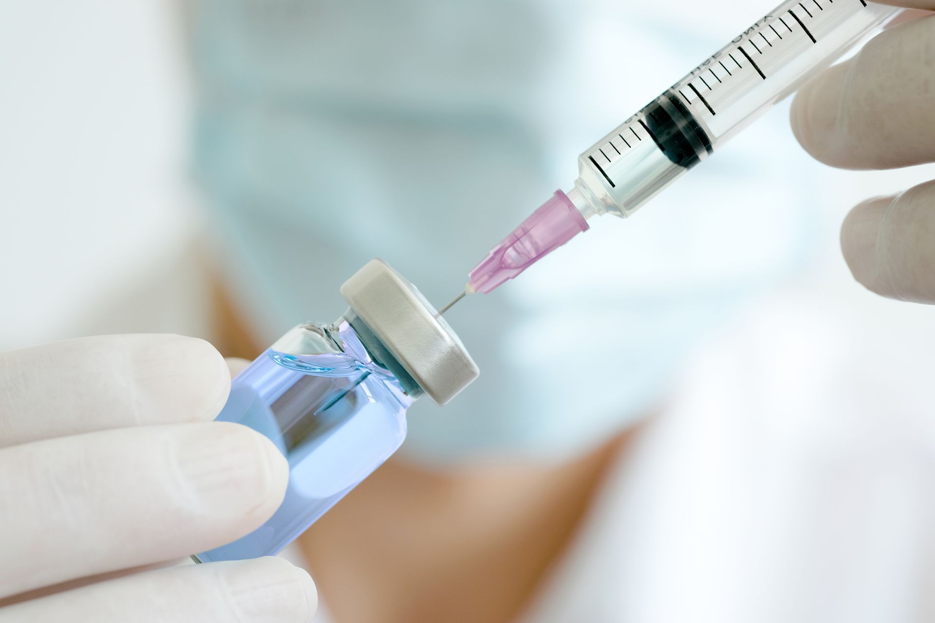A person is holding a syringe and a bottle of vaccine.