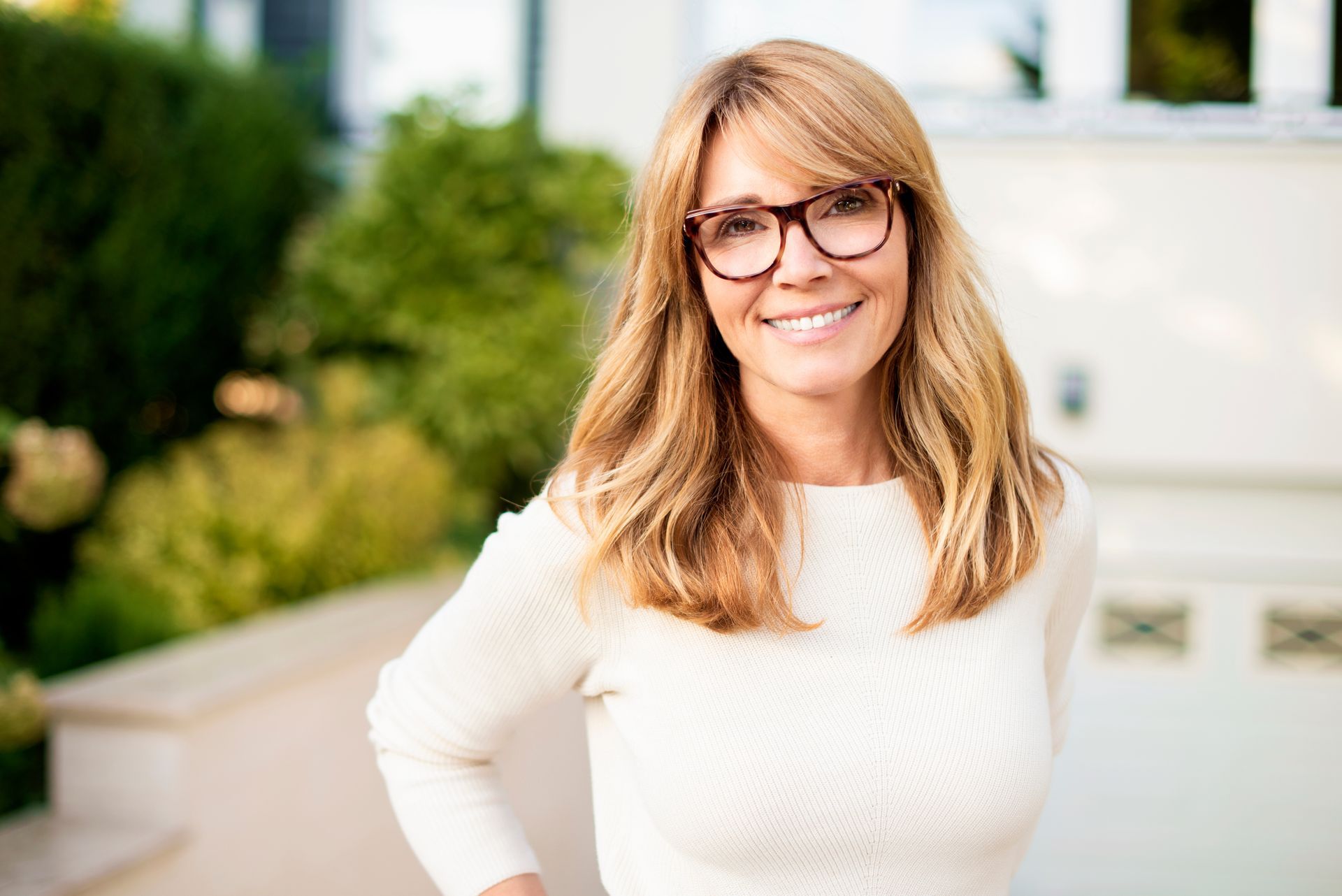 A woman wearing glasses and a white sweater is smiling for the camera.