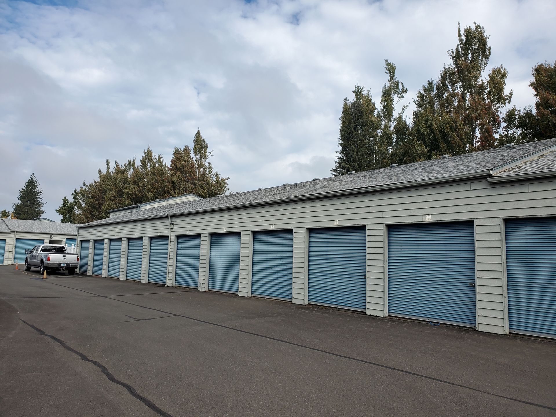 Storage units with black roll-up doors, set against a blue sky, on a paved lot. Storage units with black roll-up doors, set against a blue sky, on a paved lot.