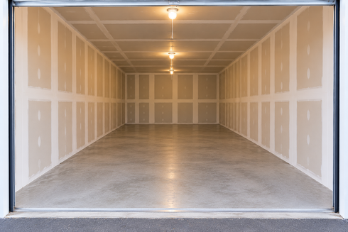 Woman pulling a cart with cardboard boxes down a storage unit hallway lined with red units. Woman pulling a cart with cardboard boxes down a storage unit hallway lined with red units.