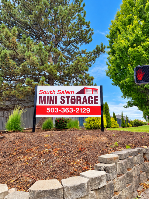 Storage unit with beige door open, filled with cardboard boxes and furniture. Storage unit with beige door open, filled with cardboard boxes and furniture.