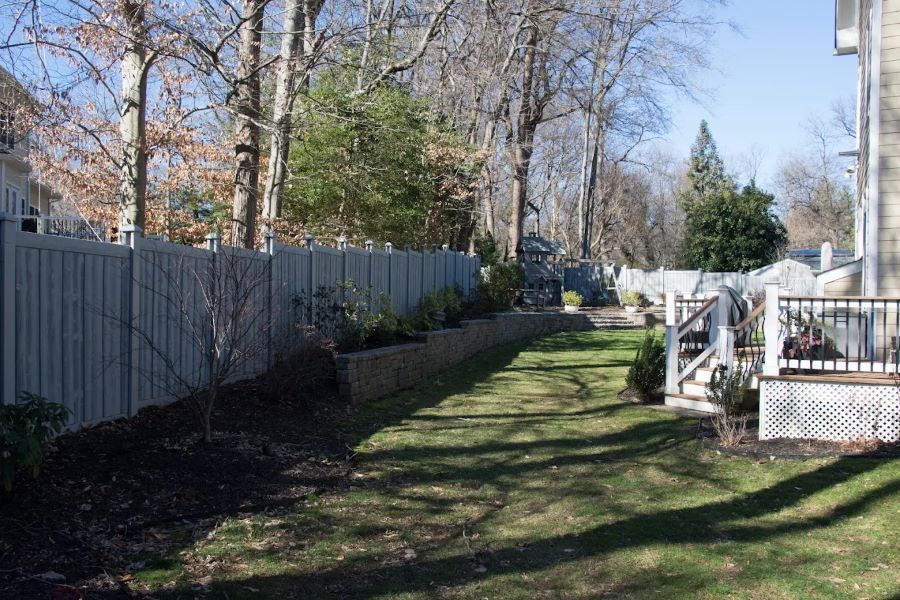 Backyard with wooden fence, grass, and a deck. Trees line the background.