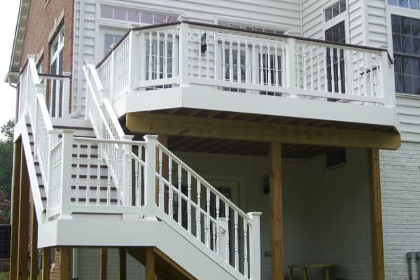 White wooden deck with stairs attached to a house with white siding and brick.