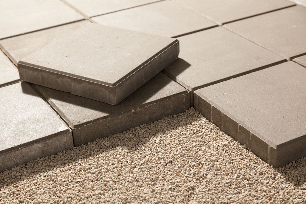 Close-up of gray paving stones being laid on a bed of gravel, outdoors.