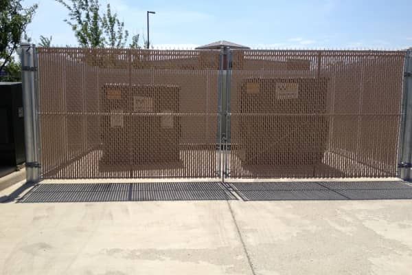 Brown metal fenced enclosure with electrical equipment, gate open, concrete surface, and blue sky background.