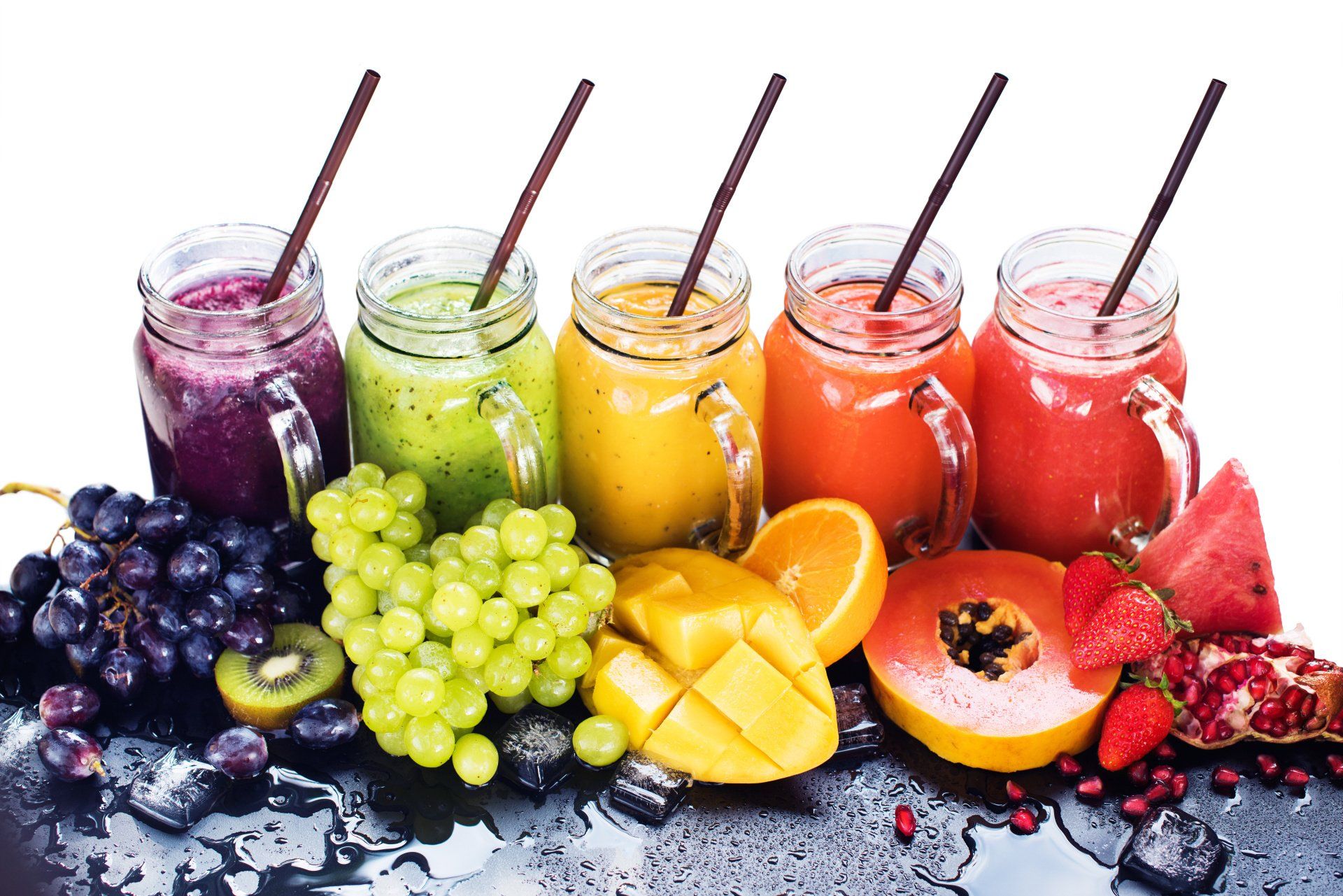 Fünf farbenfrohe Frucht-Smoothies in Gläsern mit Strohhalmen, umgeben von Weintrauben, Zitrusfrüchten, Mango, Beeren und Pfirsichscheiben.