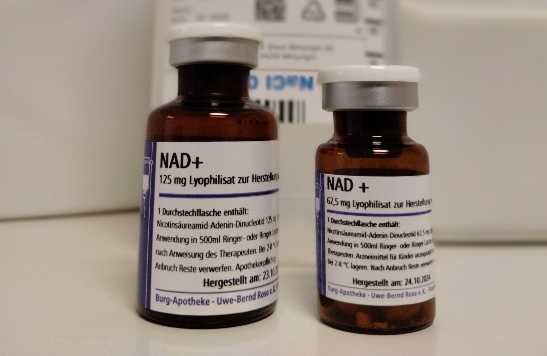 Zwei braune Nahrungsergänzungsmittelflaschen mit der Aufschrift „NAD+“ auf weißem Grund, eine große und eine kleine.