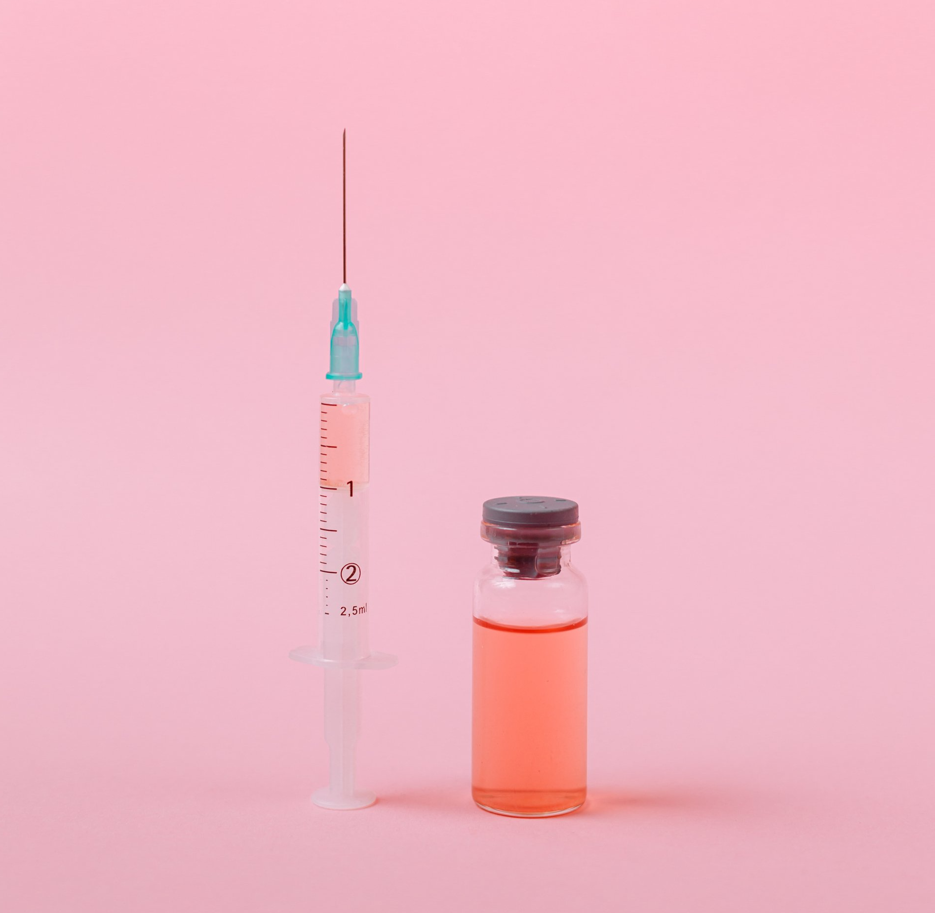 Eine Spritze neben einem kleinen Fläschchen mit rosa Flüssigkeit auf rosa Hintergrund