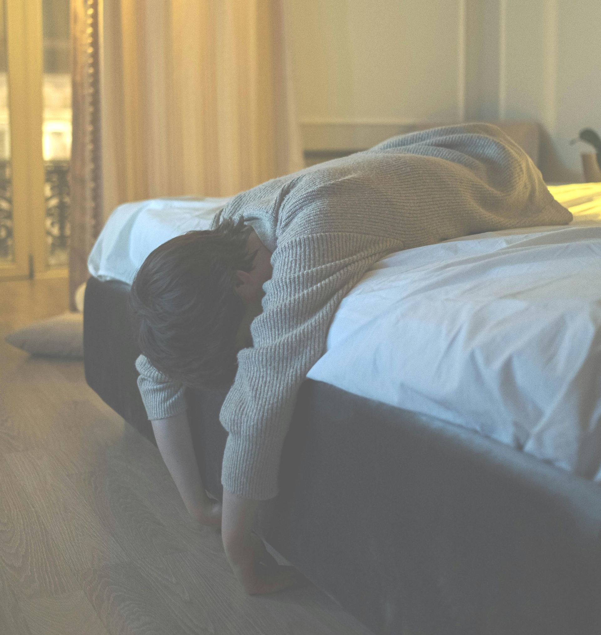 Eine Person schläft auf einem Bett und hängt teilweise über die Bettkante in einem sanft beleuchteten Schlafzimmer.
