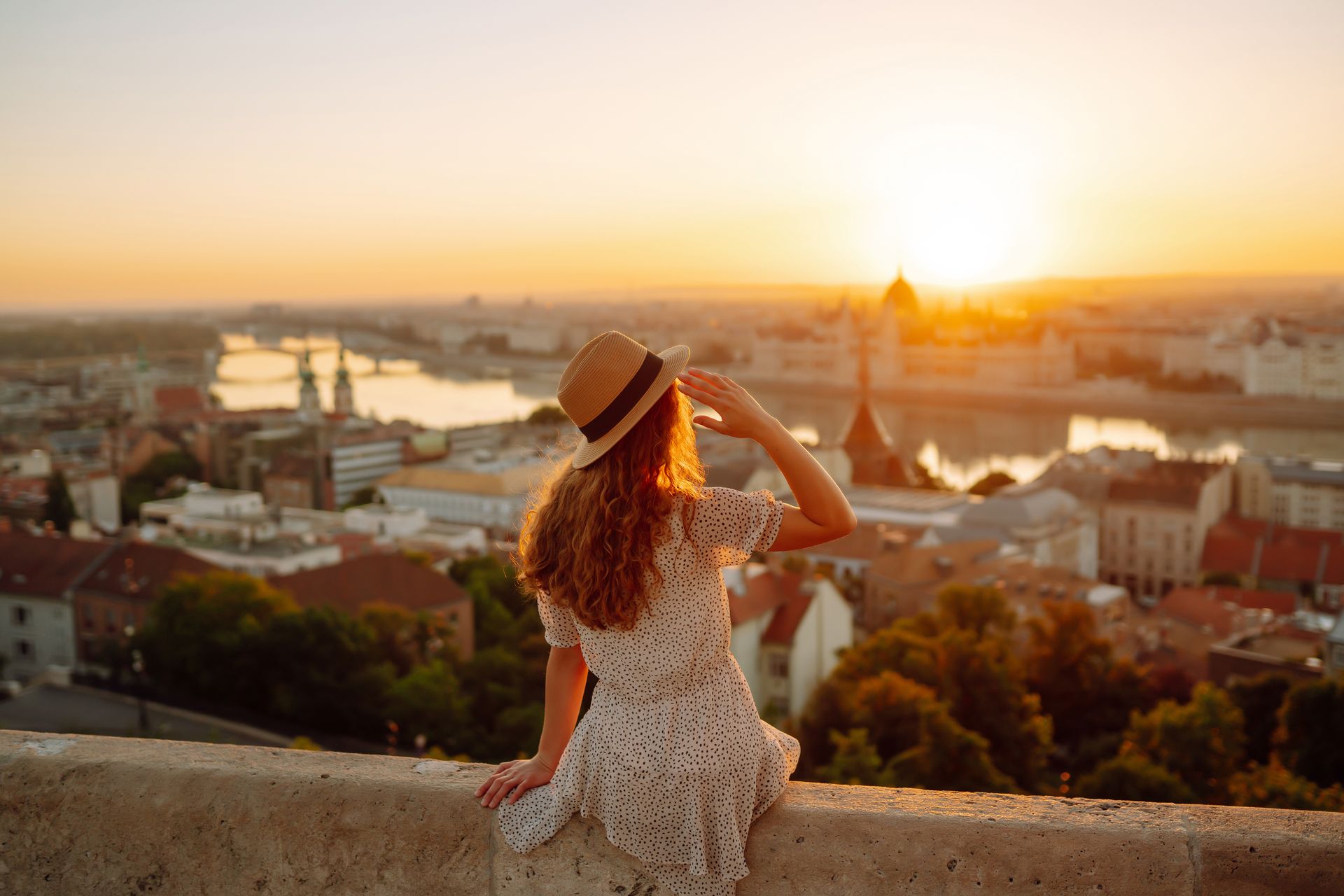 Woman in a sunhat overlooking a city skyline at sunset.