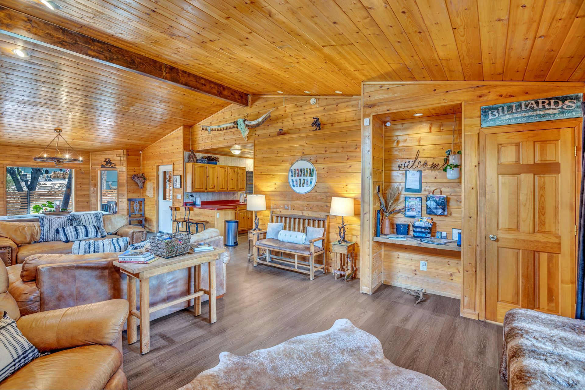 Wood-paneled cabin living room with stone fireplace, sofas, rocking chairs, and rustic decor