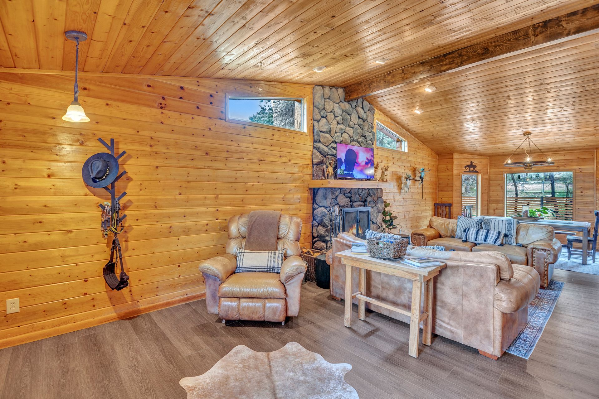 Cozy wood-paneled living room with stone fireplace, armchairs, beige sofa, and a mounted TV