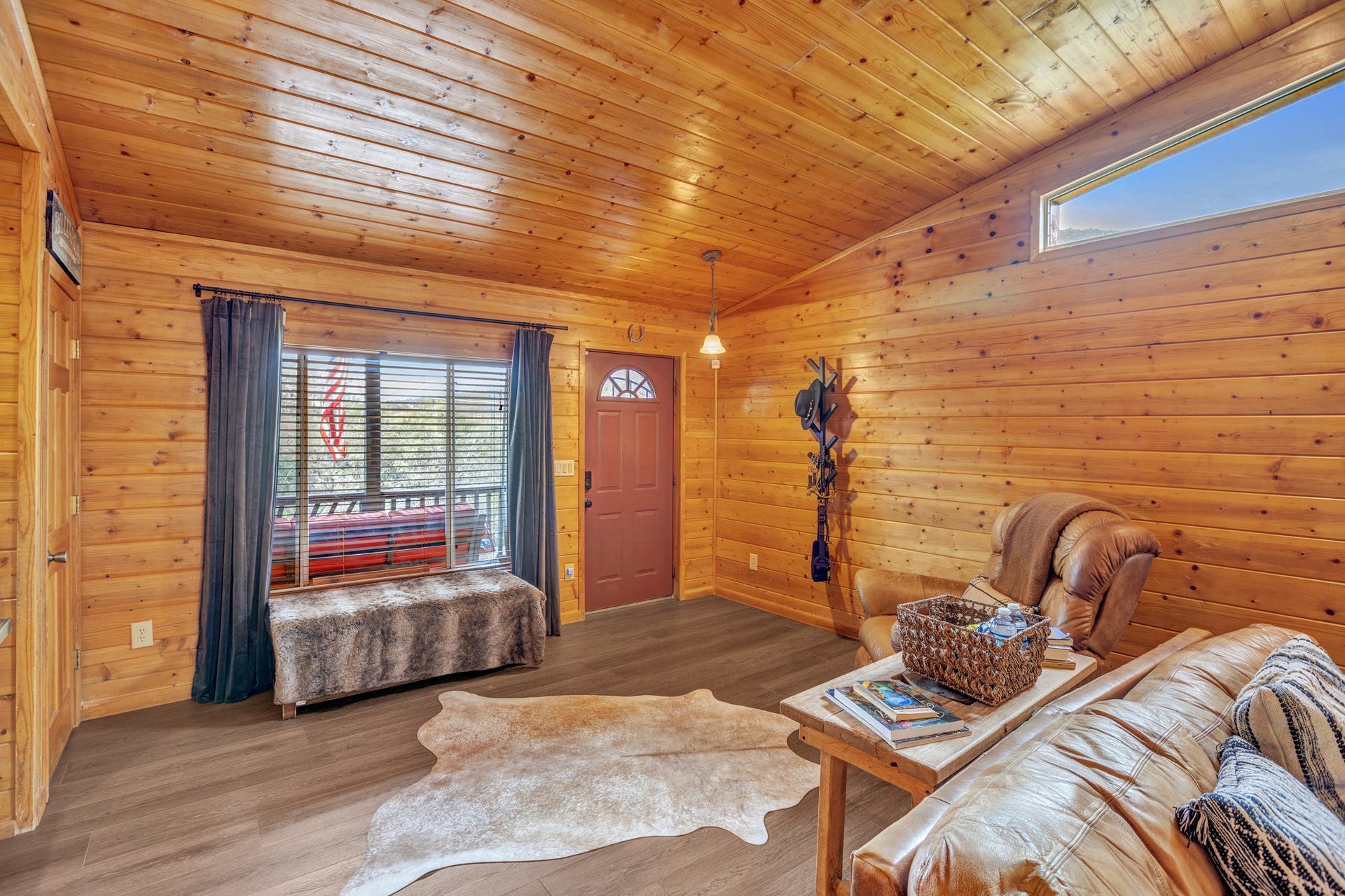 Cozy wood-paneled cabin living room with a leather sofa, rug, window seat, and small door.
