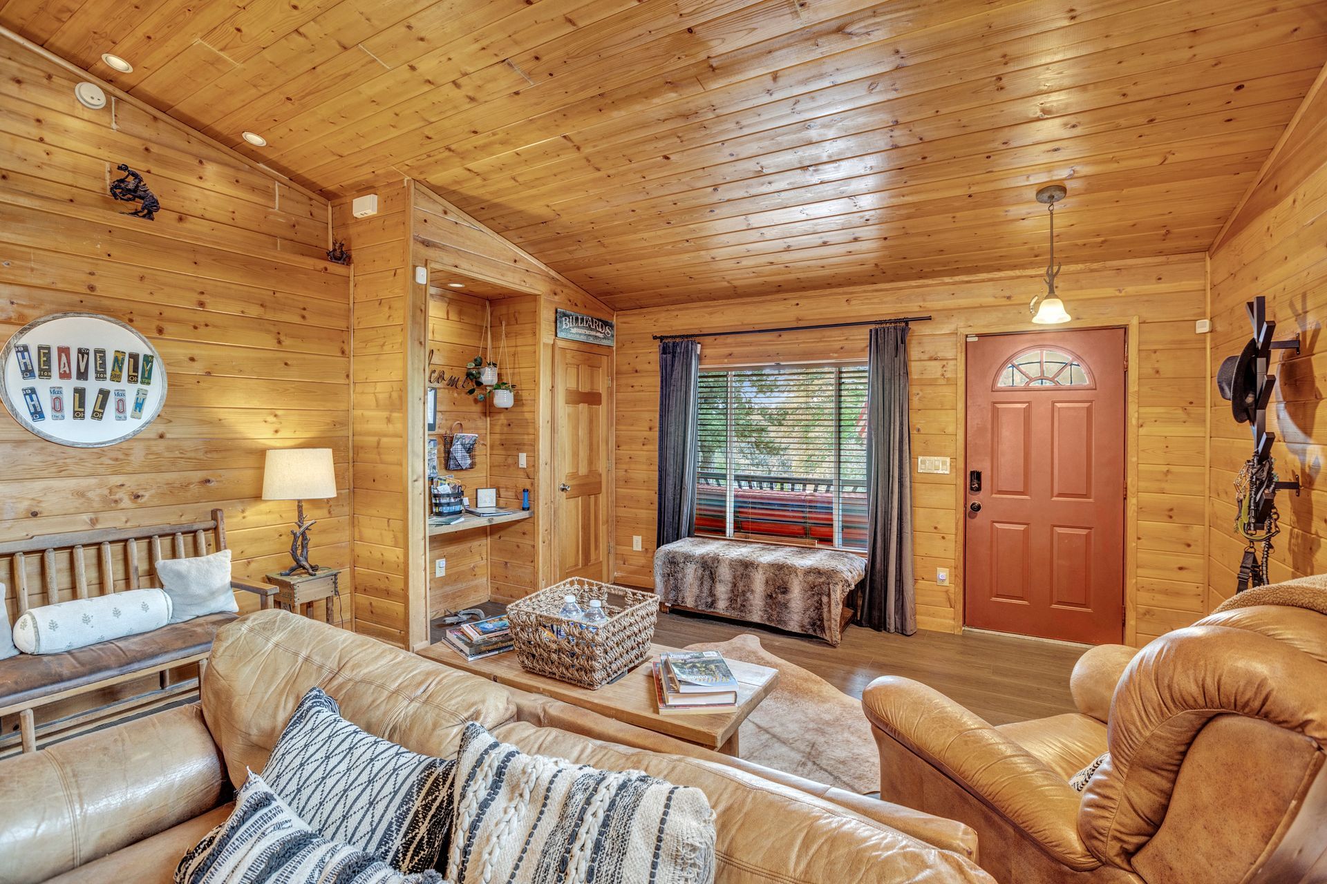 Cozy wood-paneled living room with tan sofas, patterned cushions, and a red front door