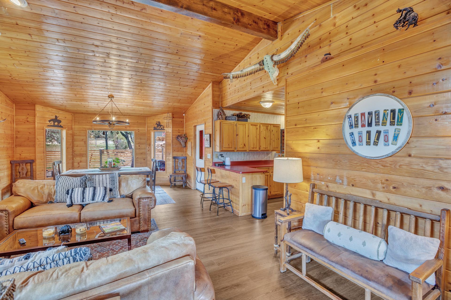 Cozy wood-paneled cabin living room with sofas, a small kitchen, and a lamp lit warmly.