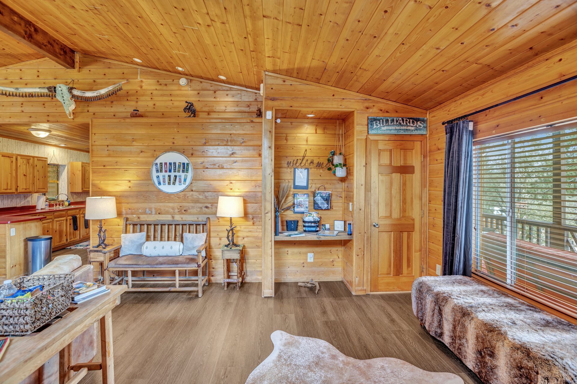 Cozy wood-paneled cabin living room with sofa, lamps, wall decor, and large window seating area