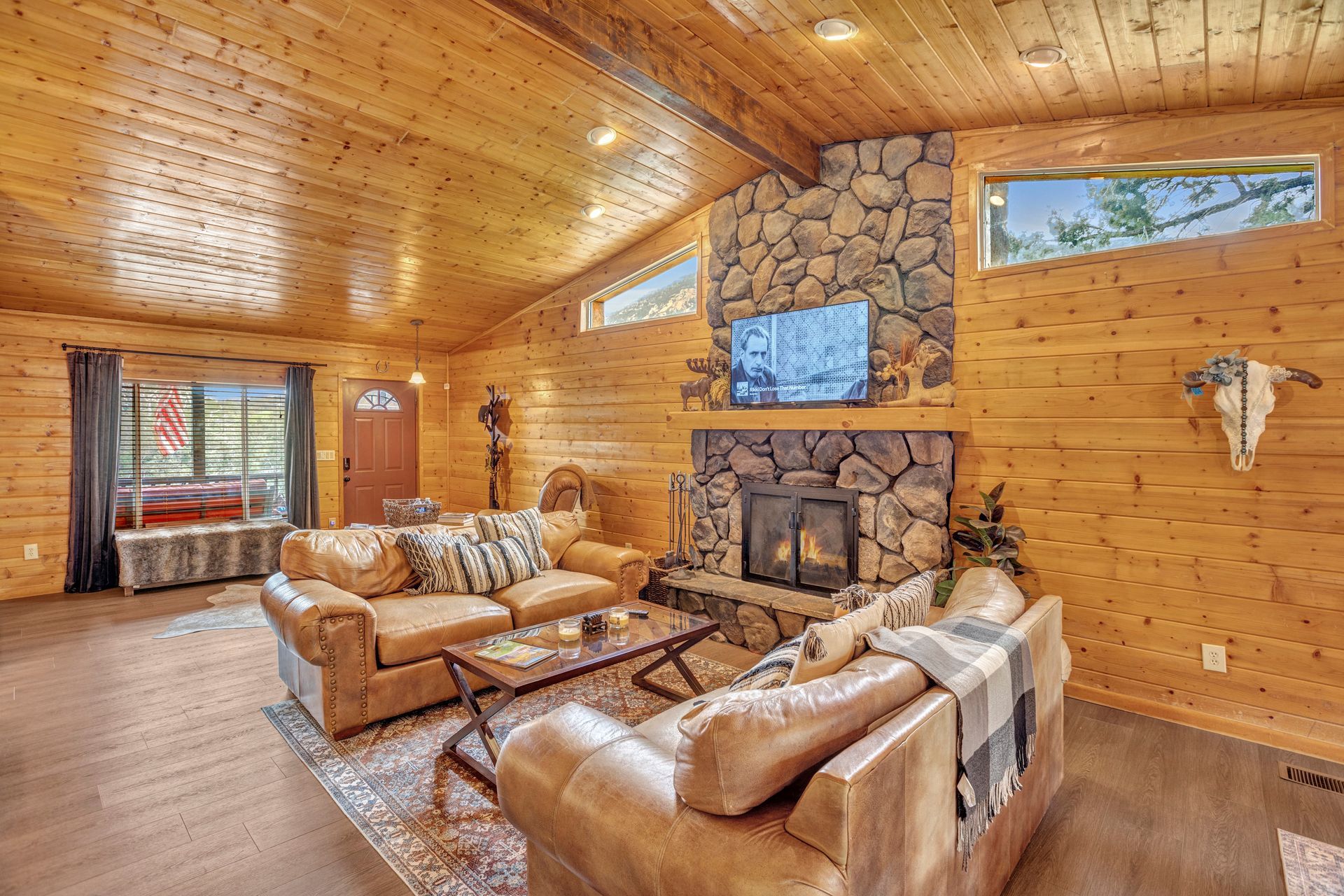Cozy log cabin living room with leather sofas, stone fireplace, and wood-paneled ceiling