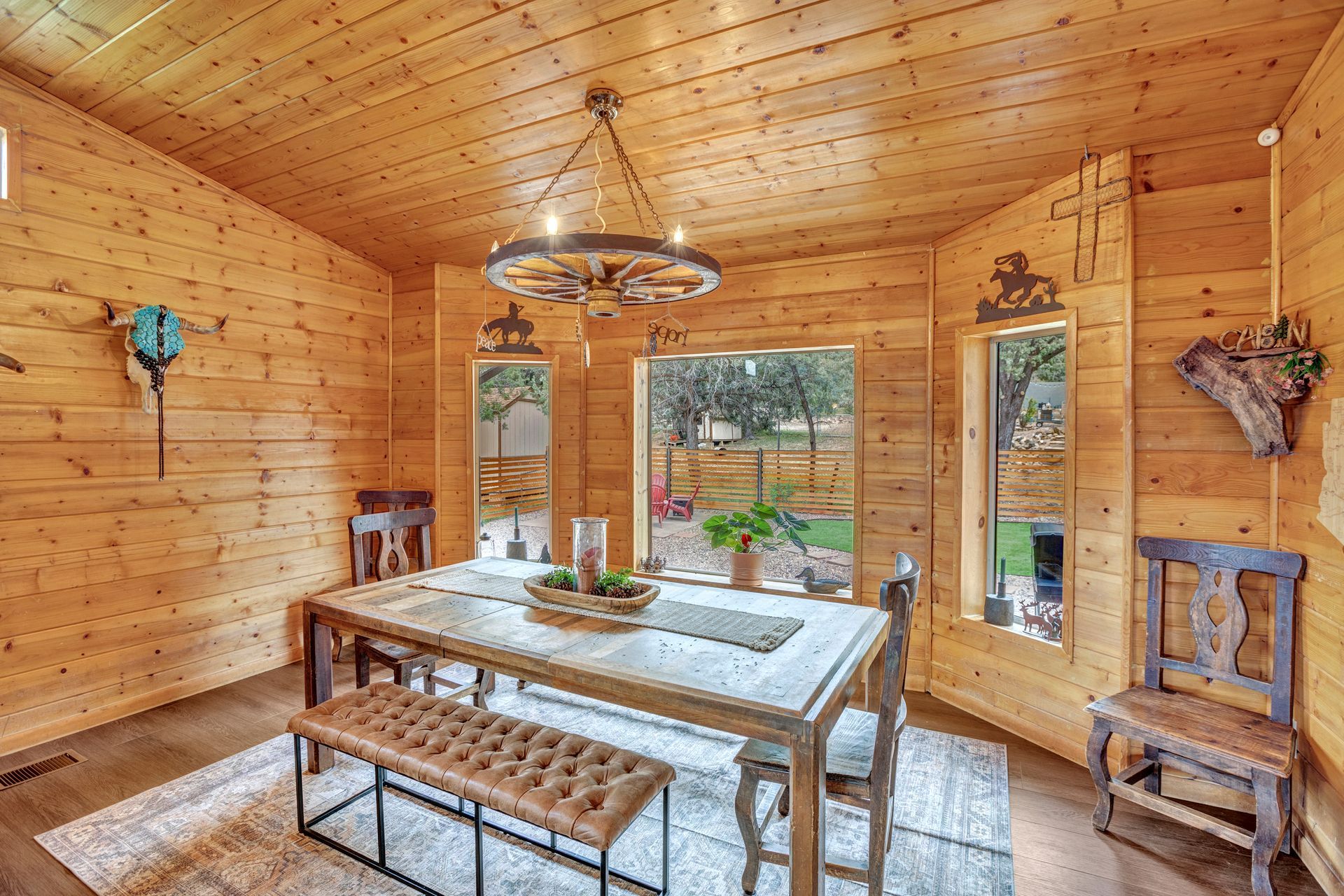Wood-paneled dining room with rustic table, bench, chairs, and large windows overlooking a garden