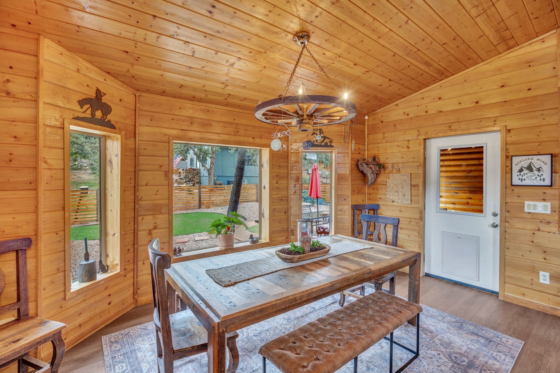 Wood-paneled dining room with rustic table, bench, chandelier, and large windows overlooking outdoors