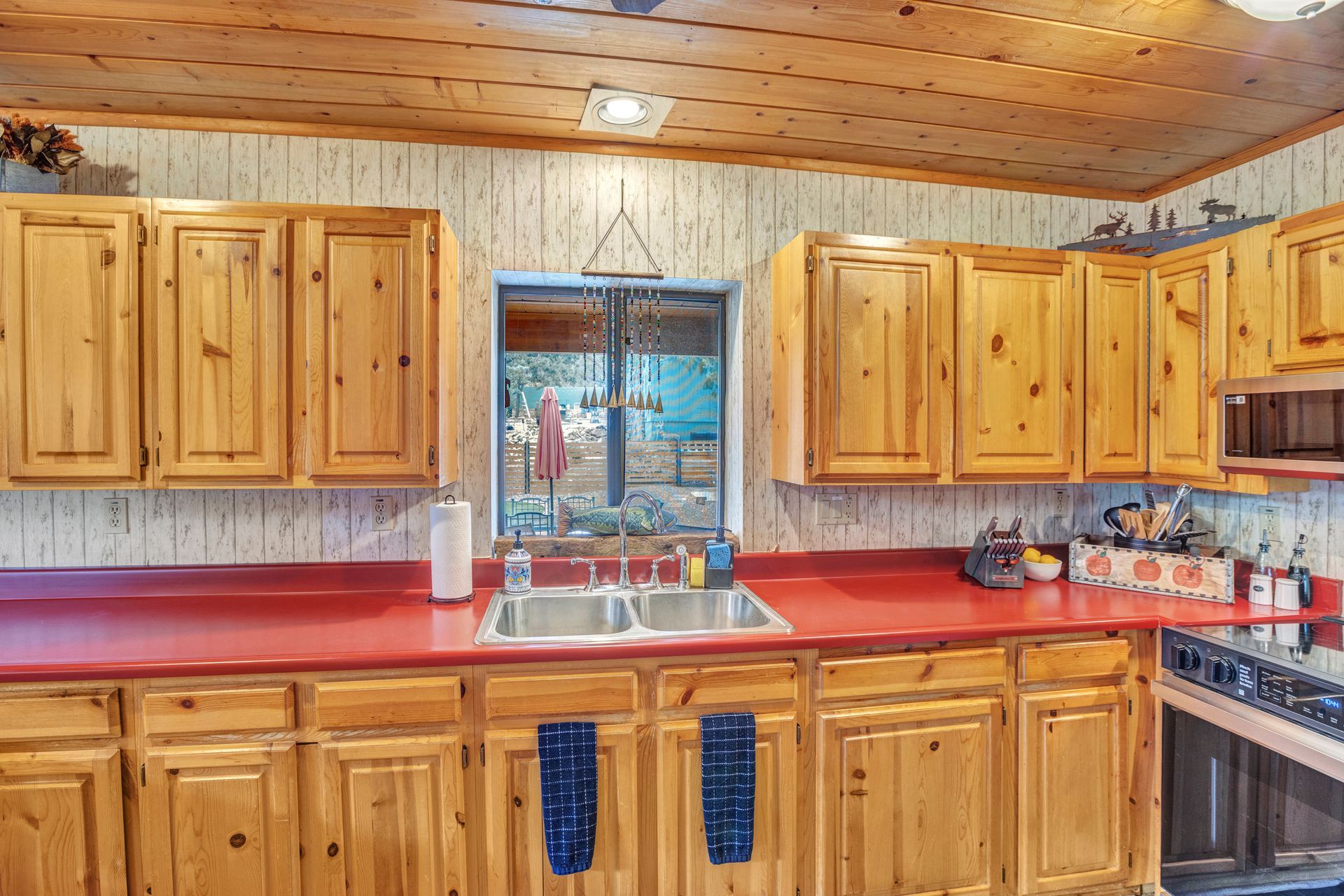 Wooden kitchen with red countertops, cabinets, and a sink centered under a window
