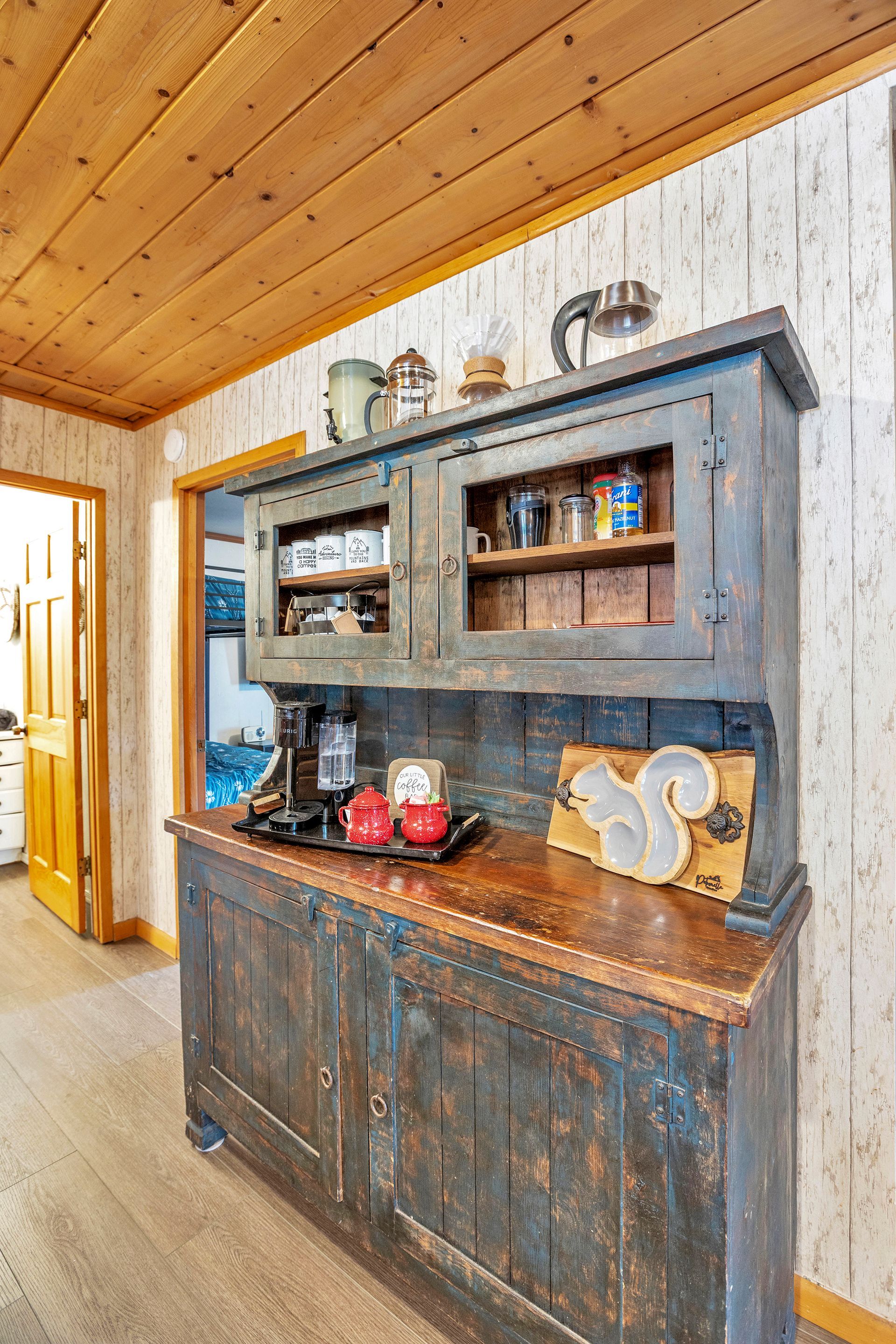 Rustic kitchen hutch with shelves, dishes, and decor against a wood-paneled wall