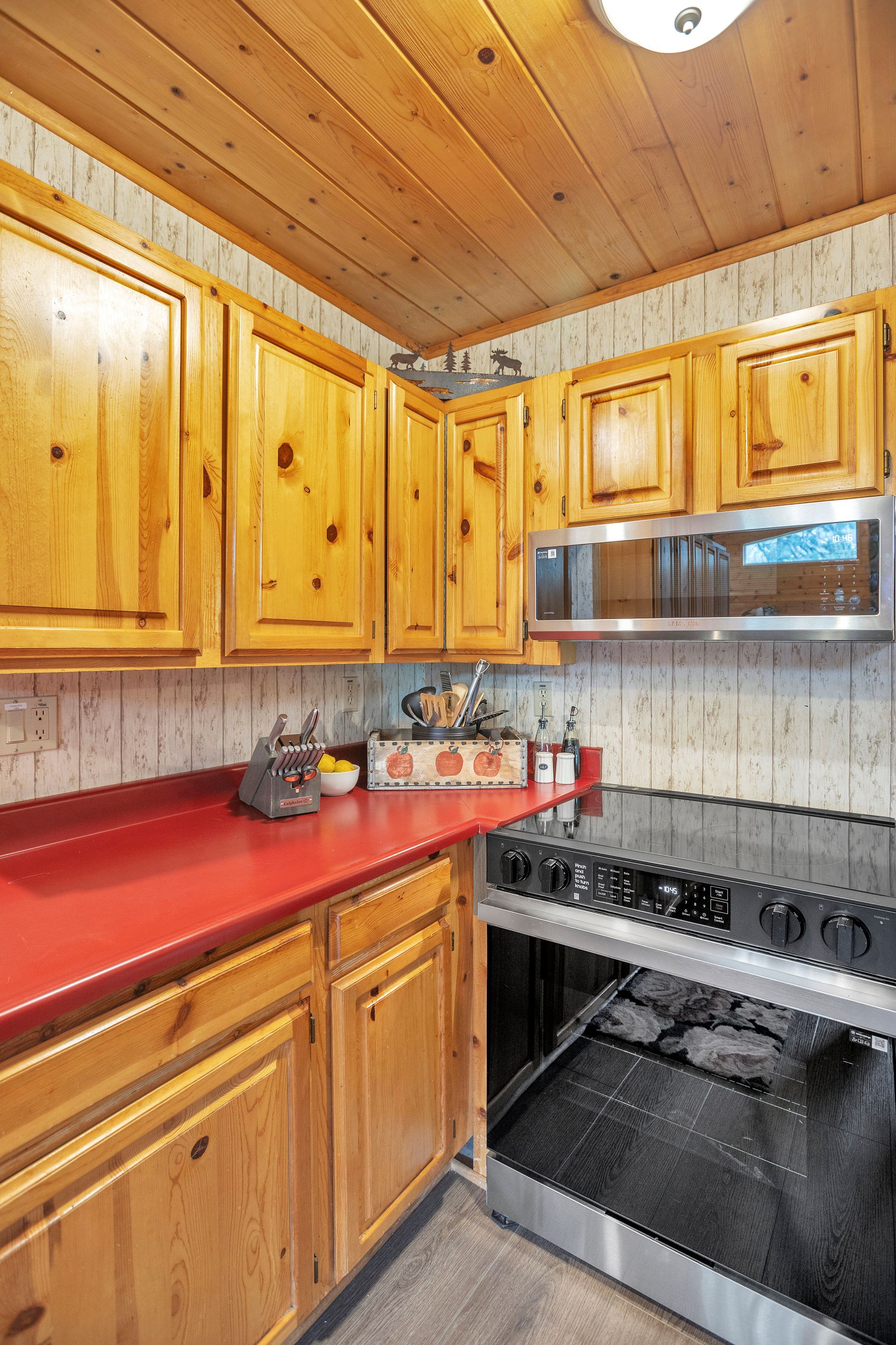 Compact kitchen with honey wood cabinets, red countertop, and black stove beneath a stainless microwave.