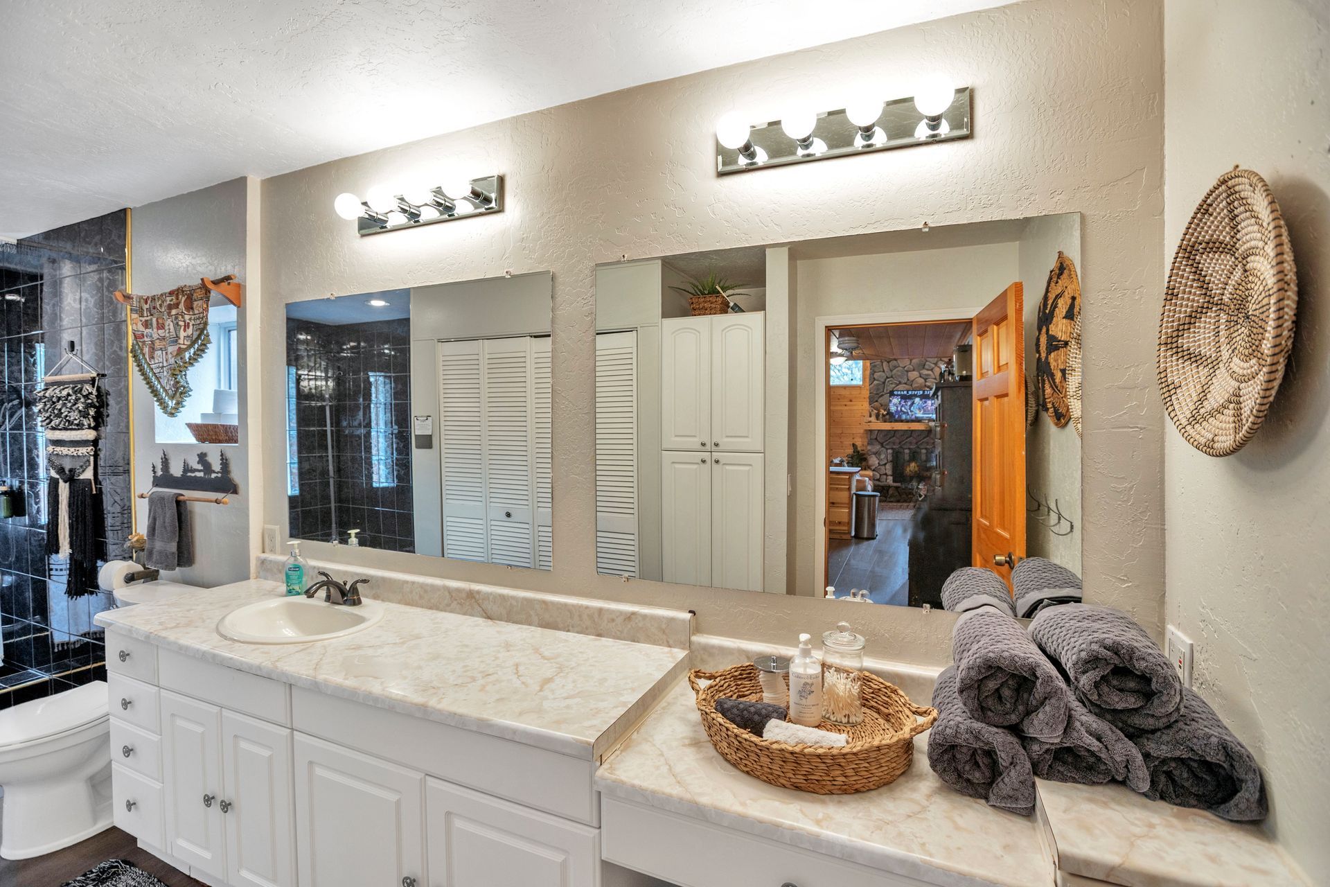Bright bathroom vanity with dual mirrors, white cabinets, marble countertop, and folded gray towels