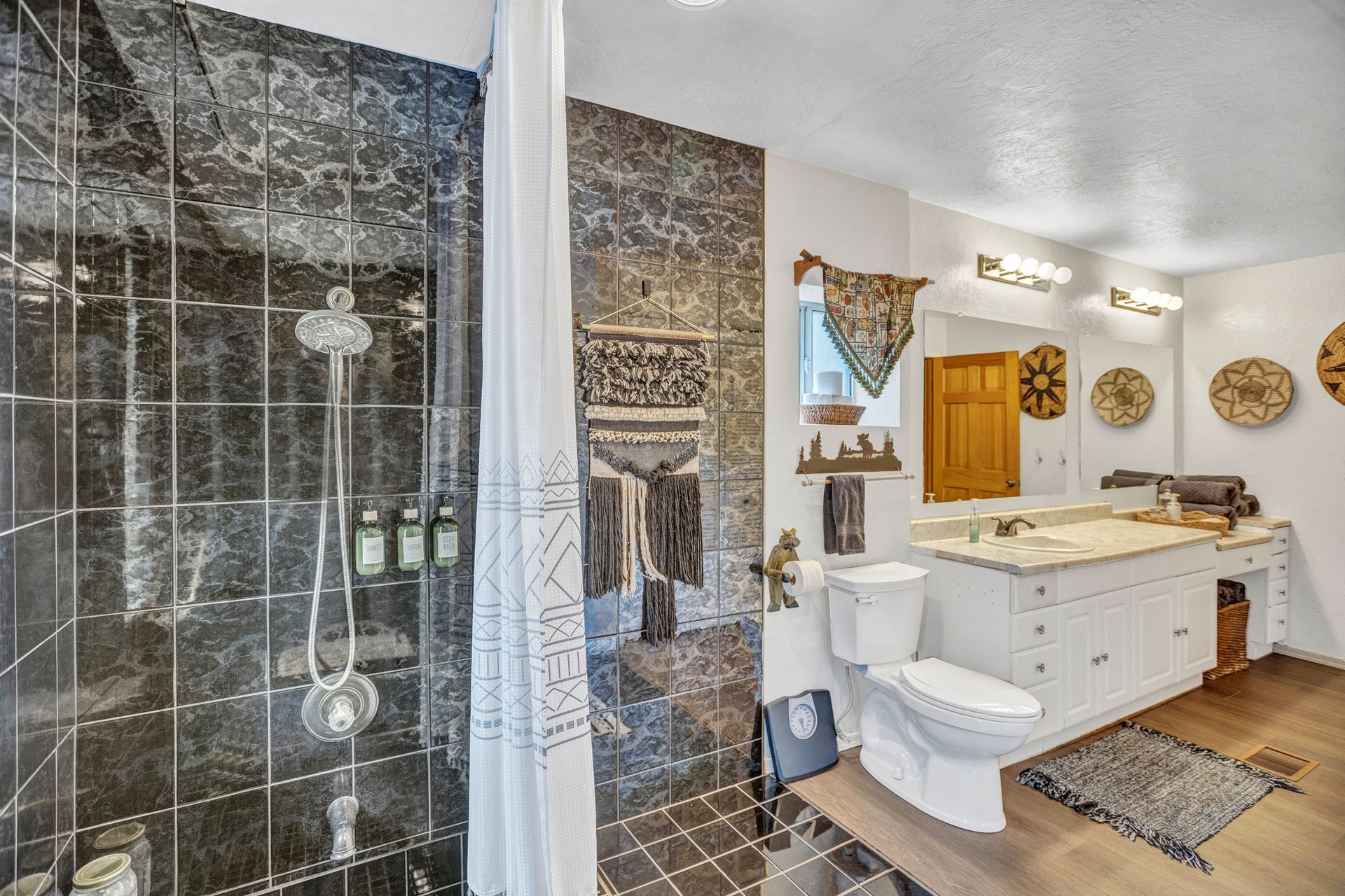 Bathroom with glass shower, dark tile walls, and a white vanity with mirror and sink.