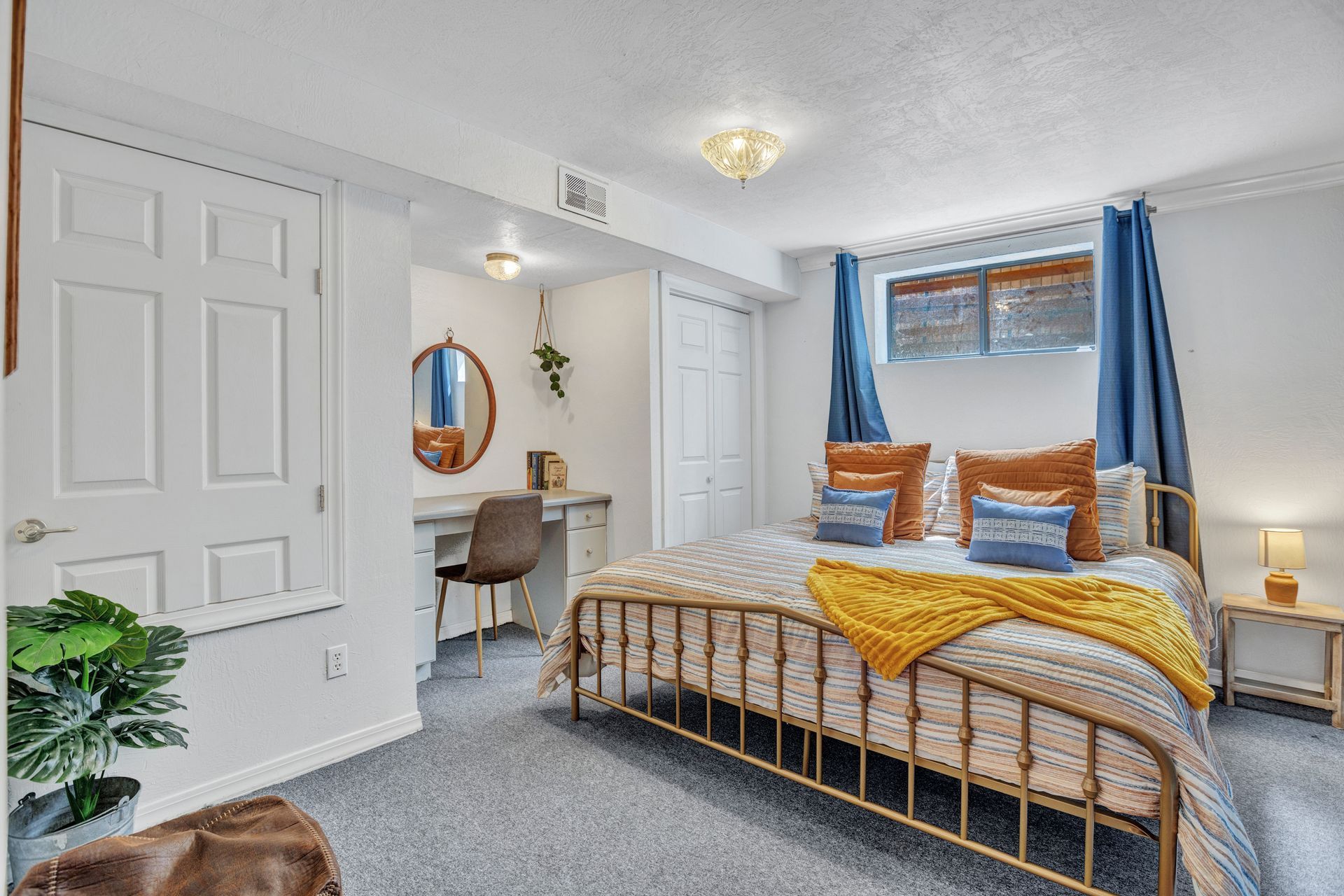 Bright bedroom with gold bed frame, blue curtains, and a small desk by the window.